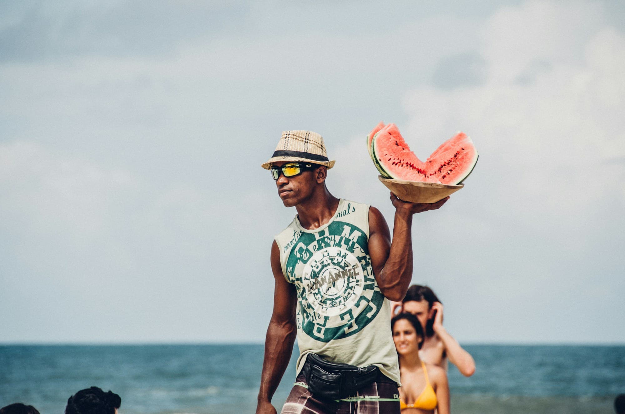 A man on the beach in Itacaré holding cut watermelon, sea and sky behind him.
