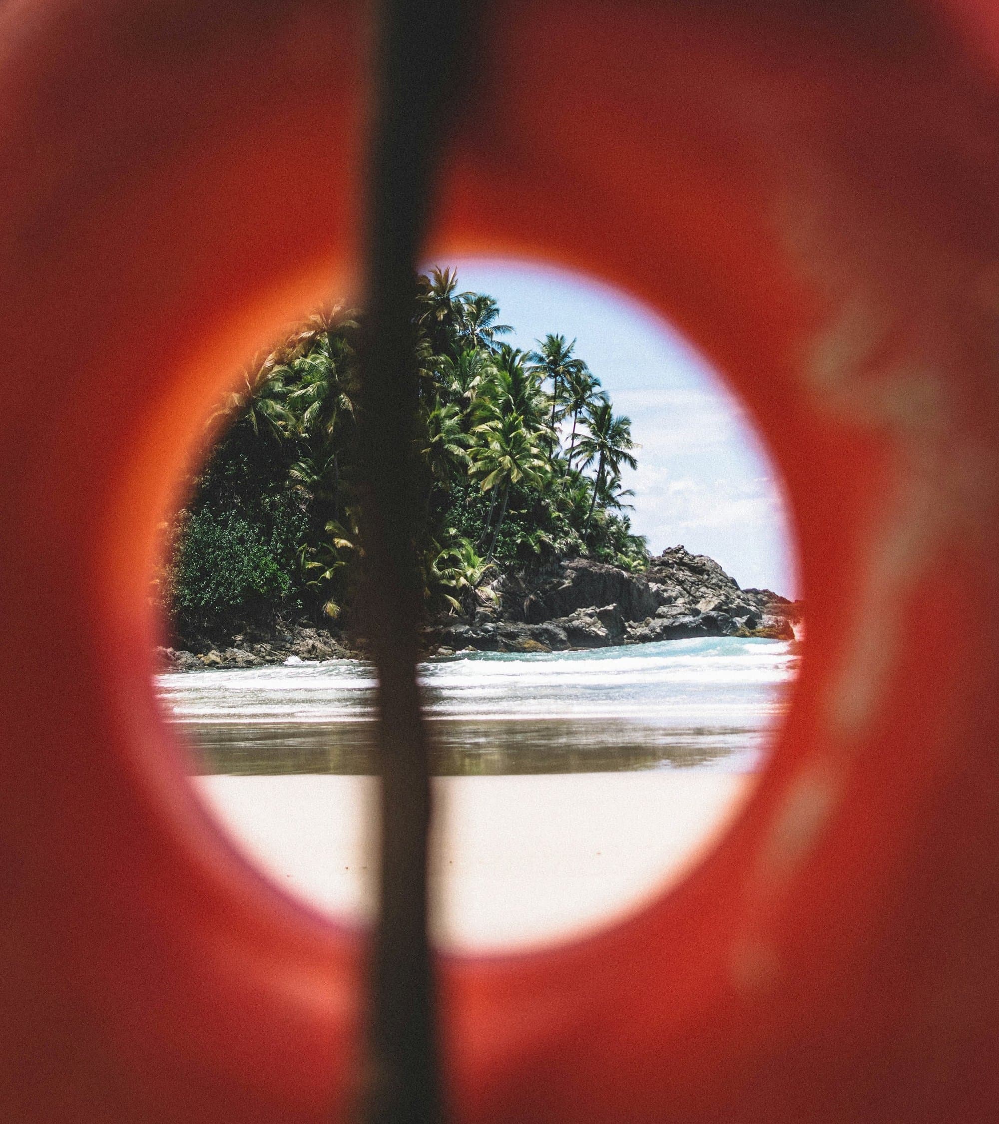A beach and a forested headland in Itacaré, seen through a round red opening.