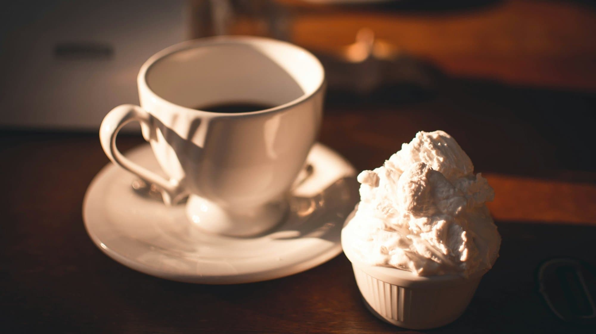 A cup of coffee and a dessert topped with cream on a wooden table in Itacaré.